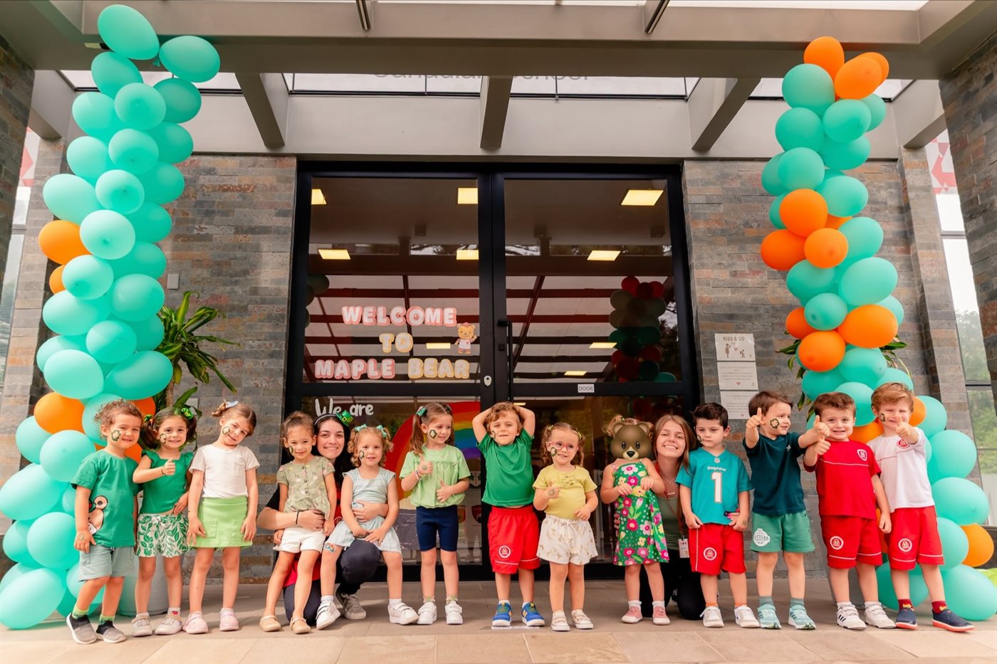 Turma de crianças da Maple Bear Bento Gonçalves reunida na entrada da escola, decorada com balões